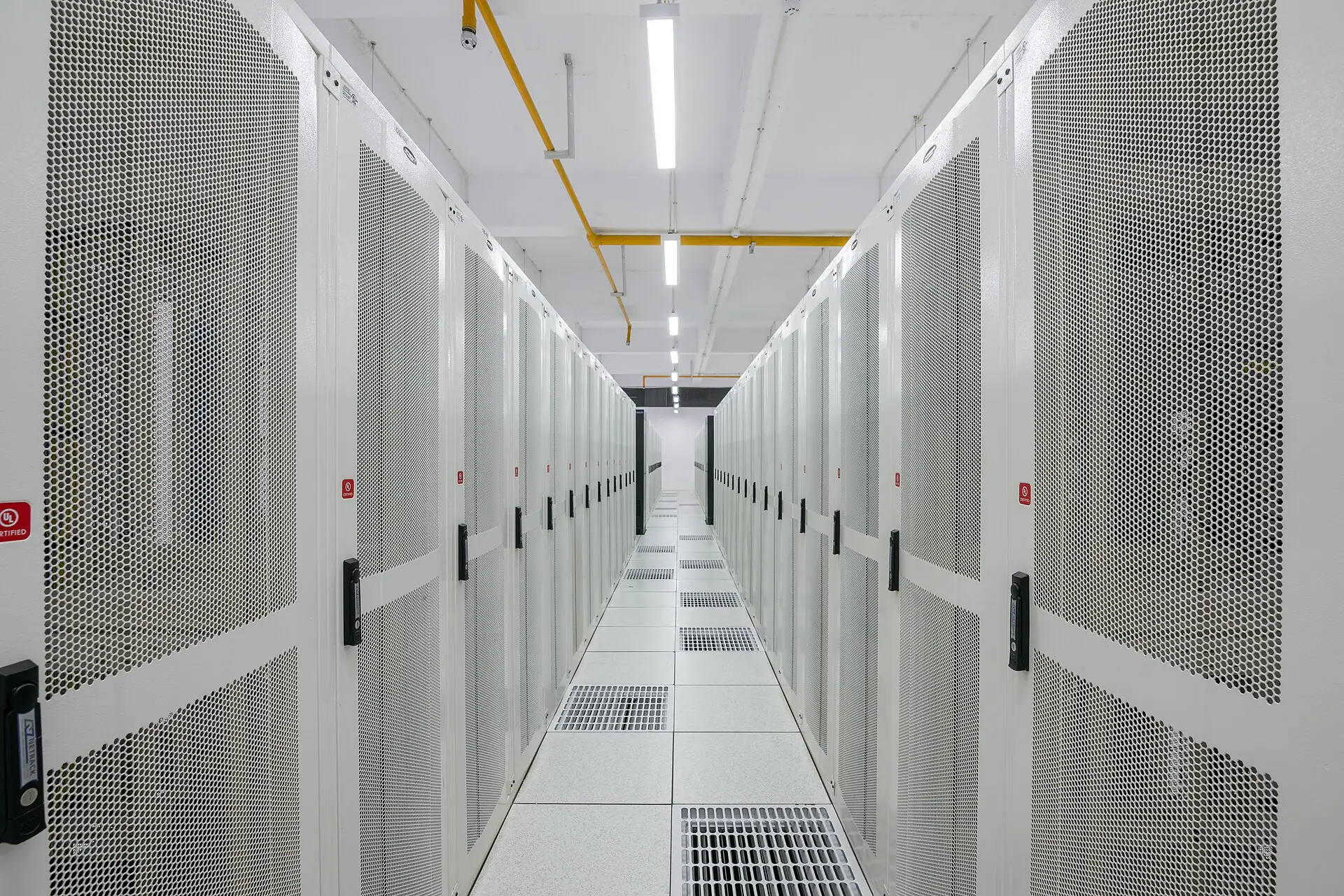 A data center aisle between rows of enclosed server cabinets above a raised floor.